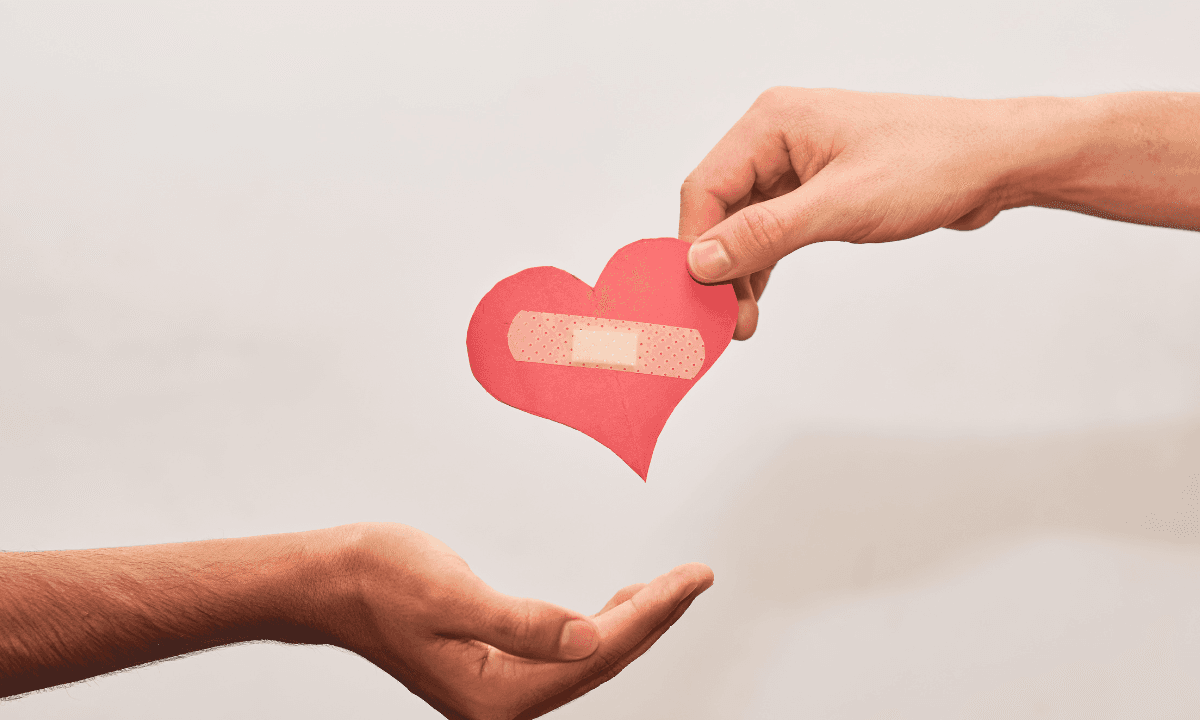 A hand offering a heart with a bandage to an open palm